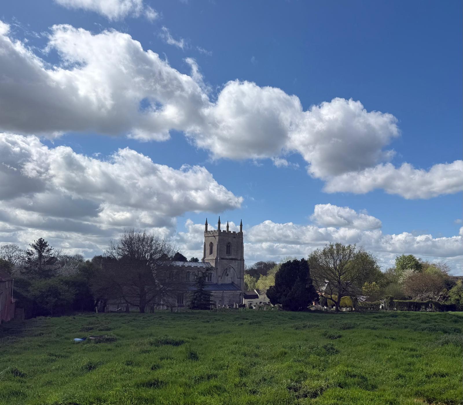 A landscape photo with a grass field, church on the horizon and blue sky.